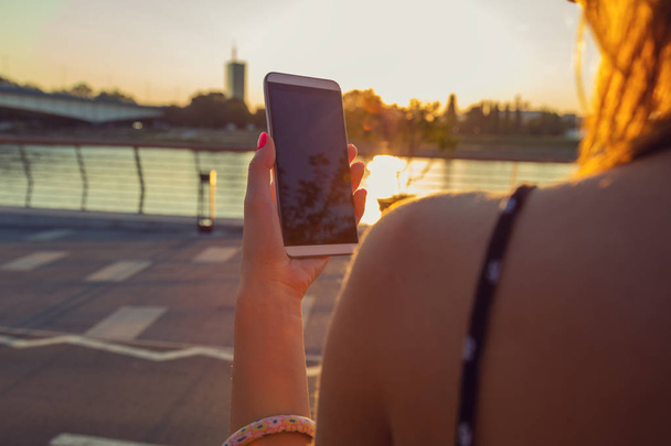 Chica usando el teléfono celular en el muelle cerca del río
. - Foto, imagen