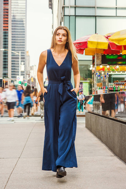 Młodzi Wschodniej Europejskiej kobieta z długich włosów brawn podróży w Nowym Jorku, na sobie niebieski bez rękawów, dekolt w serek, kombinezon, czarne skórzane buty, chodzenie na ruchliwej ulicy w middletown Manhattan - Zdjęcie, obraz