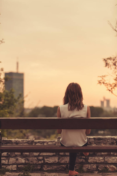 Женщина, сидящая на скамейке и смотрящая на пейзажи далекого города
. - Фото, изображение