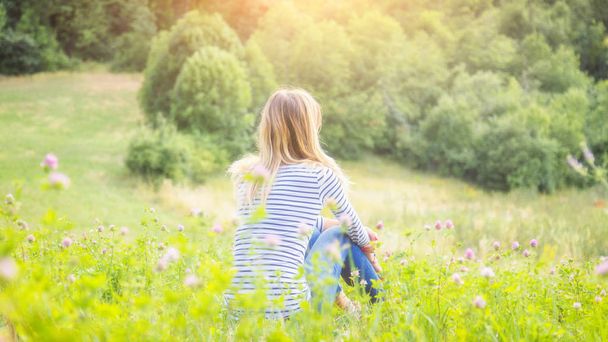 Girl sitting on a green meadow and watching the countryside landscape. - Foto, Imagem