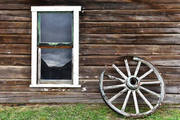 Bild eines alten hölzernen Wagenrades, das sich an eine Blockhütte lehnt.  - Foto, Bild