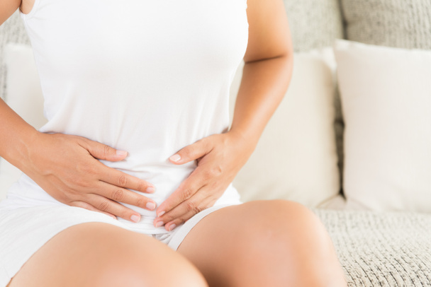 Young woman having painful stomachache sitting on sofa at home. Chronic gastritis. Abdomen bloating concept. - Фото, изображение
