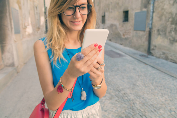Mujer linda sosteniendo el teléfono celular en un entorno urbano. El enfoque óptico está en la mano
. - Foto, imagen