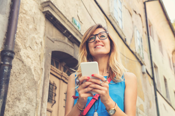 Cute woman holding cellphone in urban surroundings. - Fotó, kép