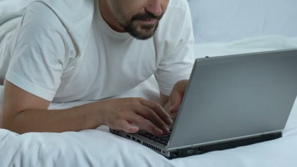 Man typing laptop lying in bed and showing thumbs up, freelancer working online - Video, Çekim