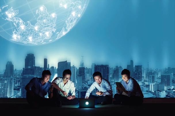 Asian business group in casual suits using smartphone, tablet and laptop for working or playing social networks and wep site on high-rise rooftop sites. Business and technology concept - Photo, Image