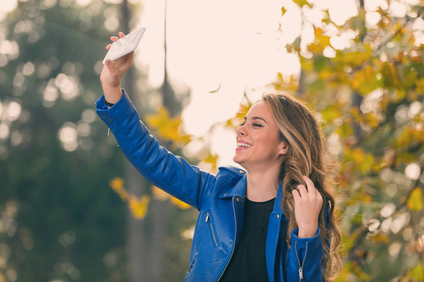 Young girl using cellphone in the park with autumn / fall colors. - Photo, Image