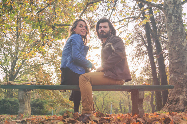 Χαριτωμένο ζευγάρι κάθεται σε ένα παγκάκι στο πάρκο γεμάτο με χρώματα του φθινοπώρου. - Φωτογραφία, εικόνα