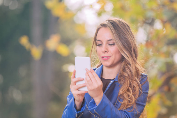 Young girl using cellphone in the park with autumn / fall colors. - Zdjęcie, obraz