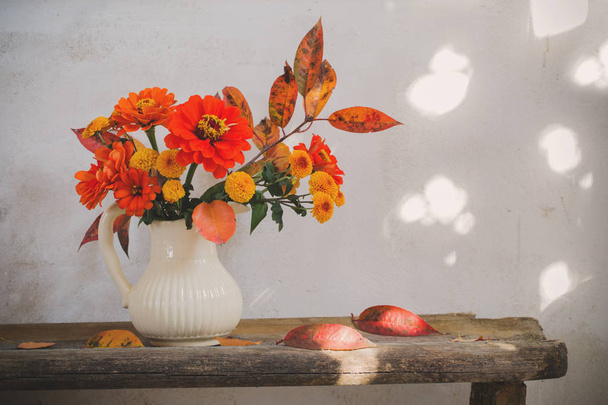 autumn flowers in pitcher on old wooden bench - 写真・画像