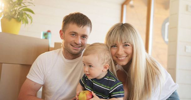 Portrait of happy family at home, sitting on floor and playing together. Mother father and child in new house spending time together. - Фото, зображення