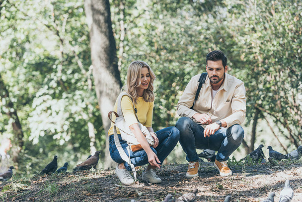 junges Paar mit Rucksack schaut Tauben im Park an - Foto, Bild