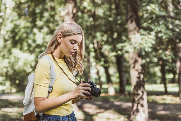 vista lateral de joven turista con cámara fotográfica y mochila en parque
 - Foto, Imagen