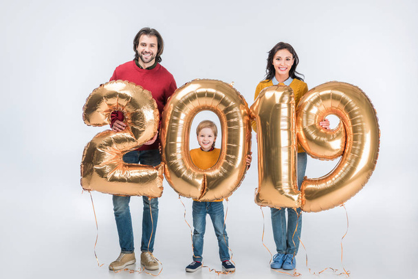 lachende ouders met zoon houden ondertekenen 2019 gemaakt van gouden ballonnen voor Nieuwjaar geïsoleerd op witte achtergrond  - Foto, afbeelding