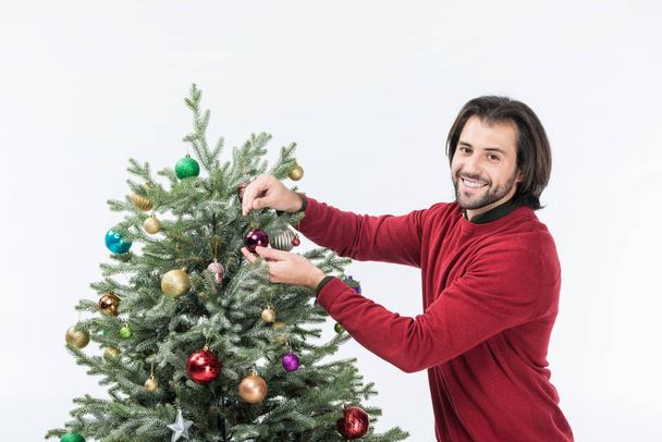 homme souriant décorant arbre de Noël avec des boules de verre et regardant la caméra isolée sur blanc
 - Photo, image