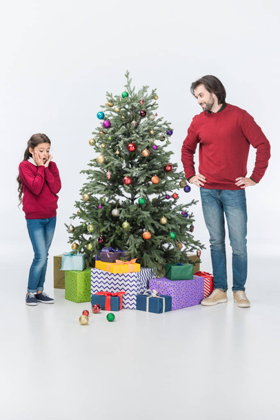 surprised daughter looking on glass balls while father standing near christmas tree with presents isolated on white - Photo, Image