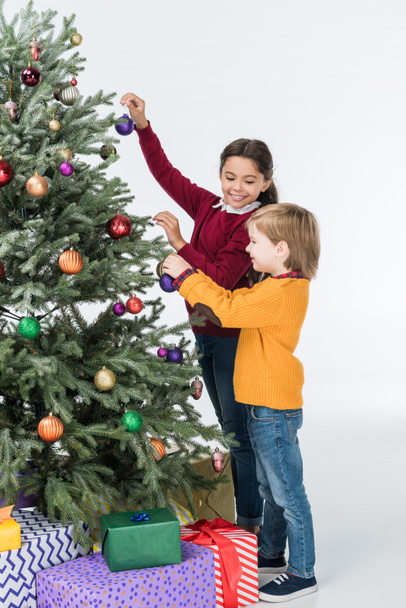 Felices hermanos decorando árbol de navidad con regalos aislados en blanco
 - Foto, Imagen