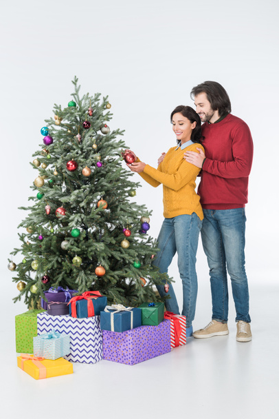 Happy husband hugging wife decorating christmas tree with presents isolated on white - Foto, afbeelding