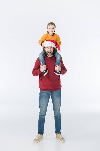 happy father in santa hat carrying son on shoulders isolated on white - Фото, изображение