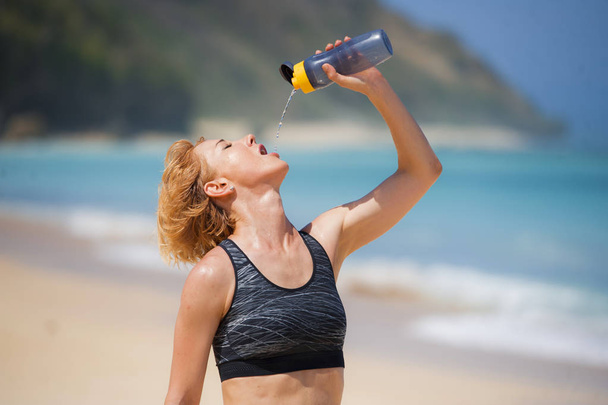 young happy and attractive sport runner woman drinking water bottle or isotonic drink after running workout at tropical paradise beach showing fit and athletic body in healthy lifestyle concept - Foto, imagen