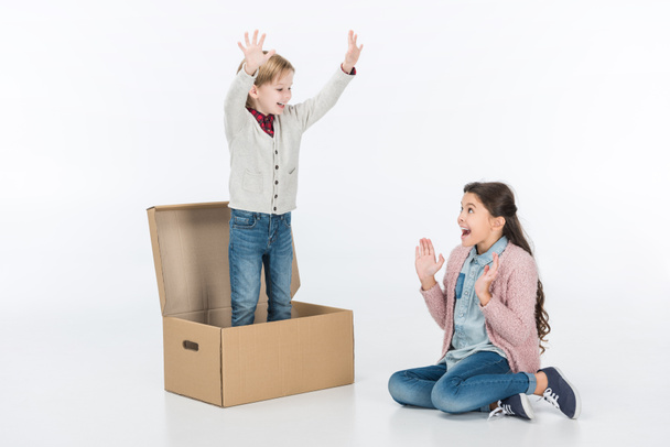 Niño sorprendido con niño de pie en caja de cartón aislado en blanco
 - Foto, imagen