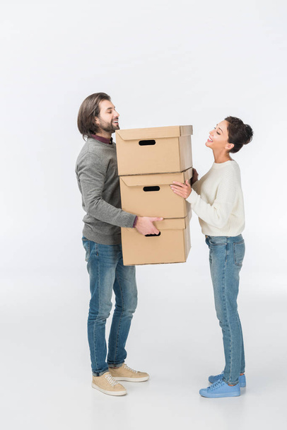 smiling couple holding stack of cardboard boxes isolated on white - Zdjęcie, obraz
