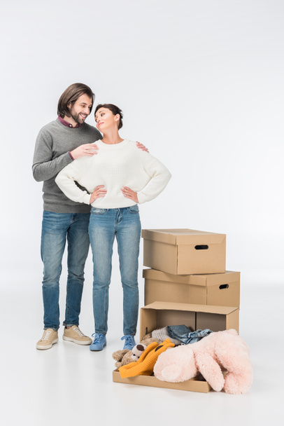 couple standing near carton box with toys and looking at each other isolated on white  - Φωτογραφία, εικόνα