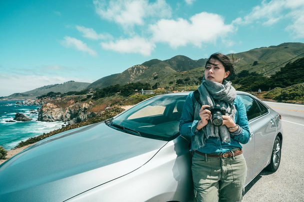 vrouwelijke fotograaf op zoek moe na een hele dag schieten en leunend op haar auto voor een pauze. - Foto, afbeelding