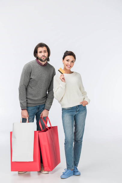 thoughtful man with shopping bags and smiling woman showing credit card isolated on white  - Foto, afbeelding