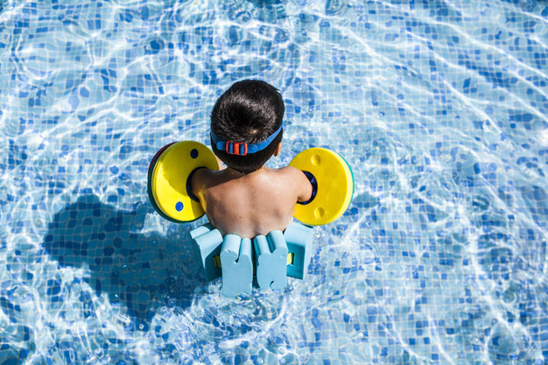 niño pequeño con carrozas disfruta de la piscina en un día caluroso de verano, vista aérea
 - Foto, imagen