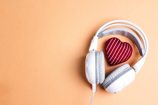 White headphones with red knitted heart and copy space. Top view, flat lay. St. valentine day composition. love music, listen to your heart concept. - Photo, Image