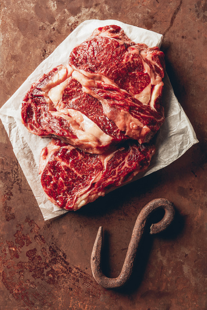 pohled shora na syrové maso steaky a kovový háček na povrch v kuchyni - Fotografie, Obrázek