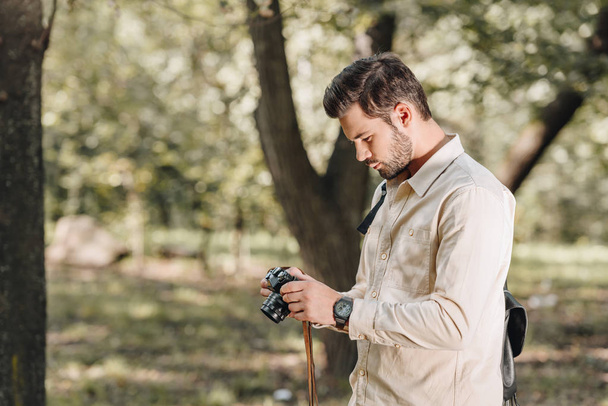 Zijaanzicht van de toerist met fotocamera in handen in herfst park - Foto, afbeelding