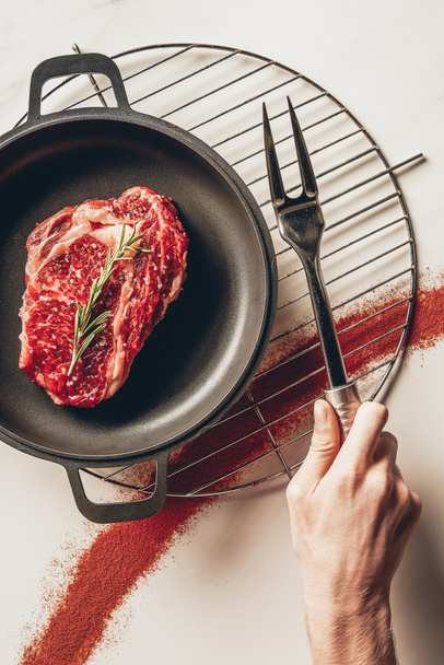 cropped image of man holding meat fork and cooking steak with rosemary in kitchen - Photo, Image