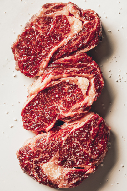 top view of three pieces of raw meat steaks and salt on white surface - Fotoğraf, Görsel