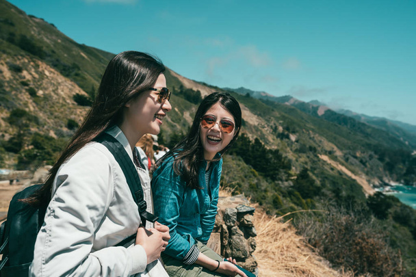 close sisters laughing together happy and sitting on the cliff surround by mountains. - Foto, Imagem