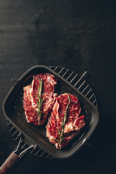 top view of raw steaks with rosemary on grill pan in kitchen - 写真・画像