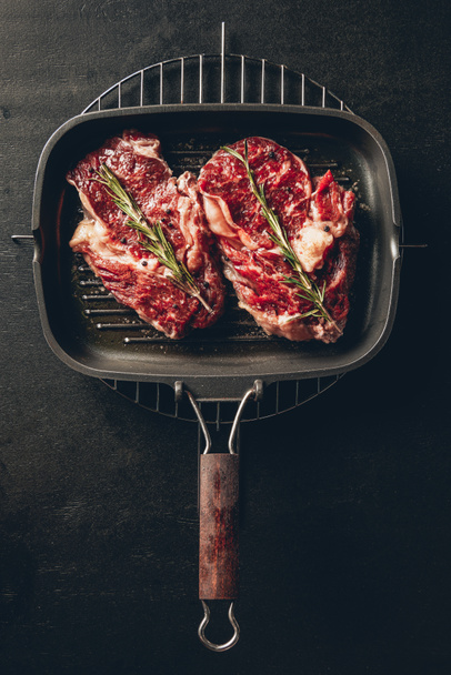 elevated view of uncooked steaks with rosemary on grill pan in kitchen - Foto, Imagen