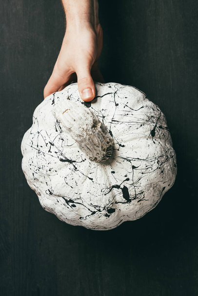 partial view of person holding white pumpkin with black paint splatters, halloween decor - Fotó, kép