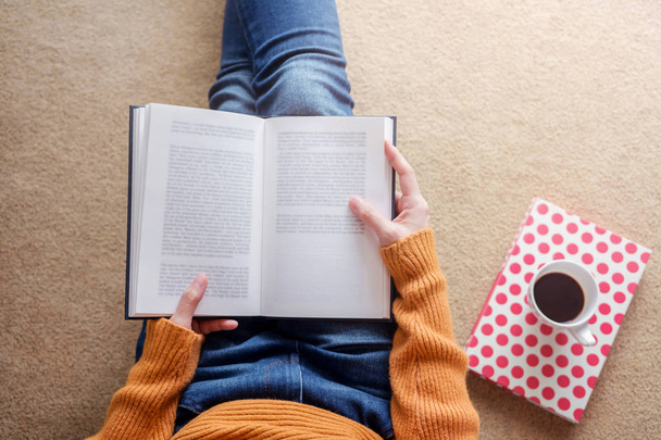 Ανάγνωση έννοιας. Μαλακή εστίαση χαλαρωτικό νεαρής γυναίκας από βιβλίο και καφέ σε φιλόξενο σπίτι, κάτοψη - Φωτογραφία, εικόνα
