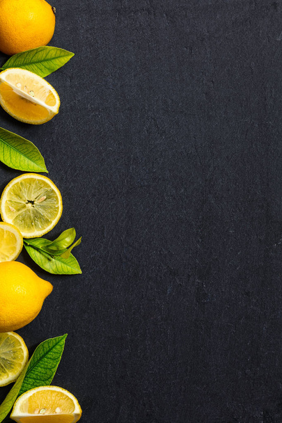 暗い石のテーブル上の新鮮なレモン。コピー空間と緑の葉の上面から熟したレモン - 写真・画像