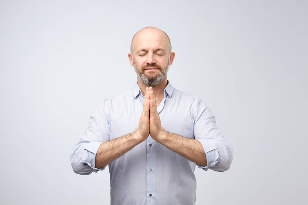 Joga i medytacja w biurze w ciągu dnia pracy. Przystojny łysy mężczyzna z włosia utrzymanie oczy zamknięte podczas medytacji, czuje się zrelaksowany, cichego, spokojnego trzymając ręce na znak mudra. - Zdjęcie, obraz