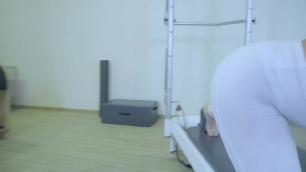 Cvičení Pilates. Žena v bílých šatech cvičí protahovací cvičení na reformátora v tělocvičně. všechny série podle čísla 01234567890001. - Záběry, video