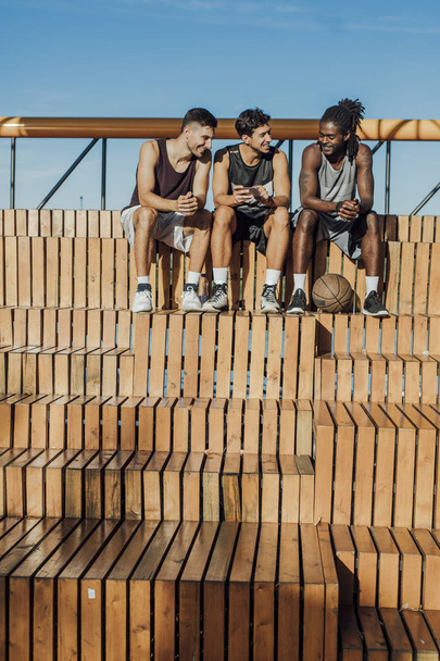 Багатонаціональна група баскетболістів, які сидять при дворі і використовують мобільний телефон
. - Фото, зображення