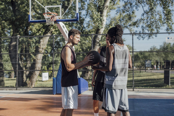 Group of young sportsmen playing basketball on outdoor court. - Foto, afbeelding