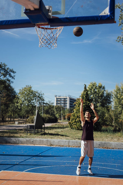Young Caucasian man playing basketball at outdoor court. - Φωτογραφία, εικόνα