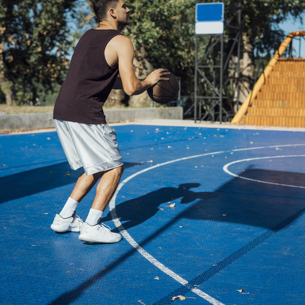Young Caucasian man playing basketball at outdoor court. - 写真・画像