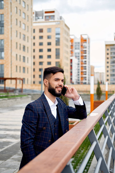 Bearded businessman speaks by phone and laughs.Young attractive business man using smartphone. Businessman talking on cell phone with customers - Photo, Image