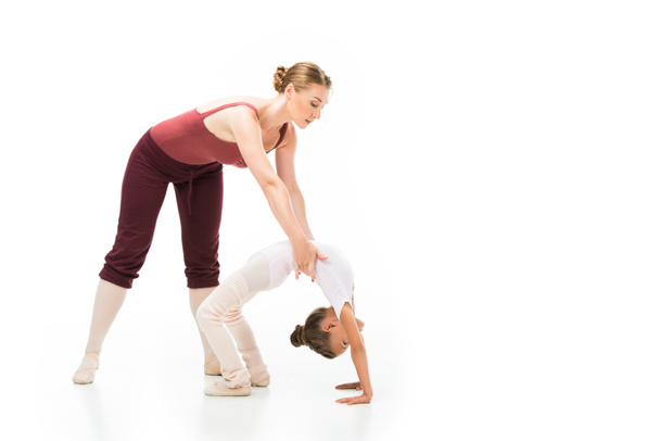 female trainer holding little kid while she doing gymnastics bridge isolated on white background  - Foto, afbeelding