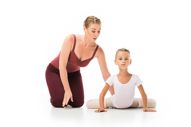 focused female trainer helping little ballerina stretching isolated on white background - Fotó, kép